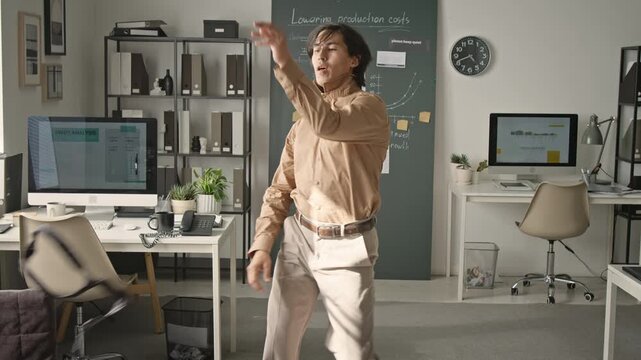 Asian young adult man dancing joyfully, removing necktie, and falling backwards in office. Ideal for corporate burnout campaigns, career change marketing, and workplace humor content