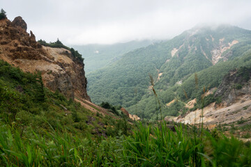 Obraz premium 霧と薄雲に包まれる夏の毛無峠と荒々しい岩肌の山岳風景