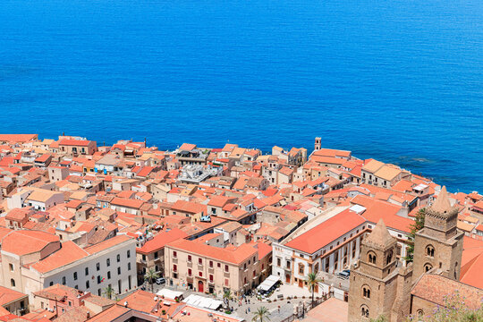 A picturesque coastal town with historic architecture and orange tiled roofs overlooks the deep blue Mediterranean Sea from above