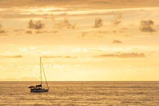 Sailboat glides across the ocean during a warm, golden sunset over the horizon