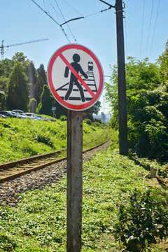 Round red prohibition sign near railway line forbidding people walking on train tracks, warning dangerous pedestrian passage zone.