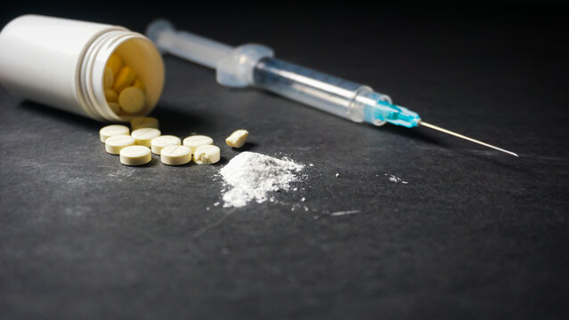 Some prescription pills spilled to black background. A syringe. Misused concept of drugs. 