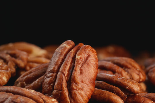 Extreme macro shot of fresh premium pecan nuts with selective focus on dark background with artistic lighting. Perfect for healthy eating, gourmet food, culinary, and dietary content.