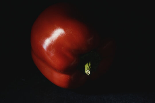 Close-up of ripe red bell pepper with vibrant green stem in moody lighting on dark background. Fresh raw vegetable for organic recipes, culinary menus, nutrition, and healthy eating.