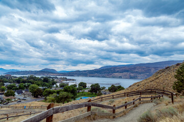 Fototapeta premium Scenic overlook of a lakeside town with rolling hills and cloudy skies, Lower Knox Mountain Shelter, Apex Trail, Kelowna, V1Y 7M8, Canada