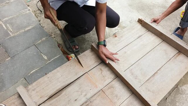 A person sawing a wooden board with a hand saw. The video shows manual woodworking activity related to carpentry, construction, home improvement, repair, and practical craftsmanship.