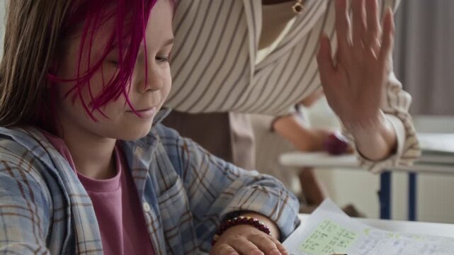 Unrecognizable teacher assisting Caucasian schoolgirl with writing assignment in classroom. Footage suited for primary education campaigns, tutoring services and learning promos