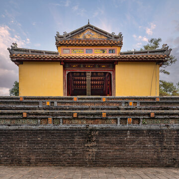 Ornate Stele Pavilion at the historic tomb of Emperor Minh Mang in Hue, Vietnam, showcasing traditional imperial architecture and intricate wall detailing under a soft sunset sky