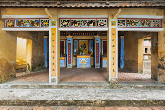 Traditional architectural details with ornate calligraphy pillars and a colorful central altar at the historic Hon Chen Shrine in Hue, Vietnam