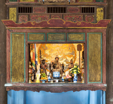Ornate wooden altar with religious statues, incense, and fruit offerings inside the Hon Chen Shrine in Hue, Vietnam