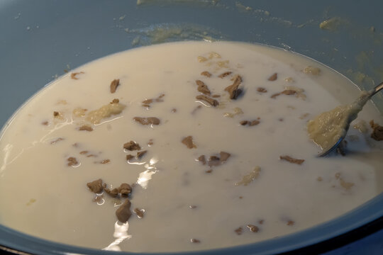 metal spoon stirring crumbled brown compressed yeast and melting butter into lukewarm white milk inside blue enamel bowl
