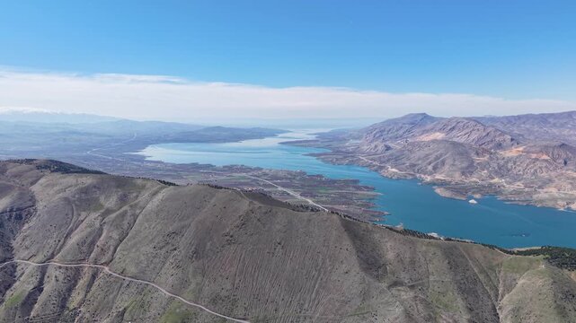 4K aerial drone shot ascending over a mountain and moving forward toward an endless blue river flowing through a majestic valley. Color grading friendly flat profile.