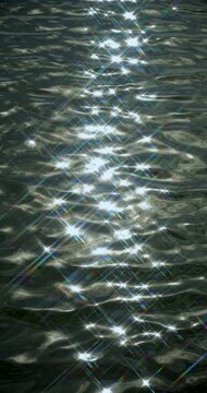 Abstract water sparkle glitters on dark rippling water surface, with clustered light reflections drifting in vertical bands. Abstract water sparkle gives water calm, luminous abstract look.