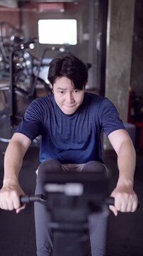 Middle aged Asian man straining while riding exercise bike during intense workout in industrial gym