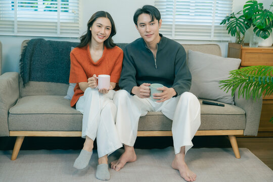 Happy Asian couple sitting on sofa talking and gesturing together at home
