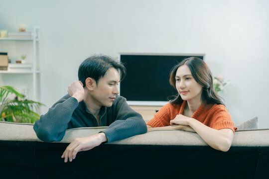Happy Asian couple sitting on sofa talking and gesturing together at home