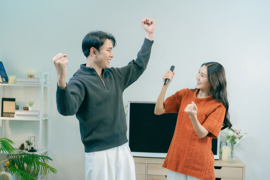 Happy Asian couple dancing and singing together in living room at home