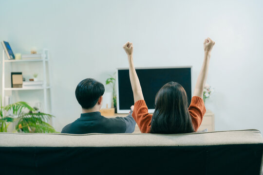 Happy Asian couple dancing and singing together in living room at home