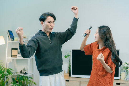 Happy Asian couple dancing and singing together in living room at home