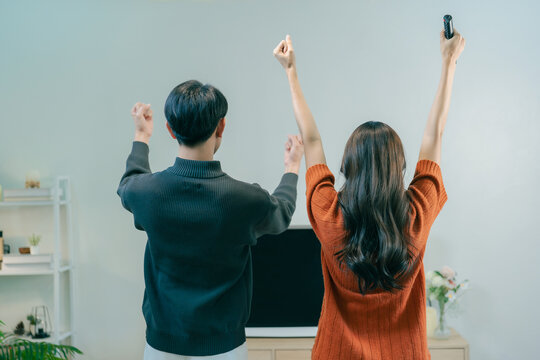 Happy Asian couple dancing and singing together in living room at home