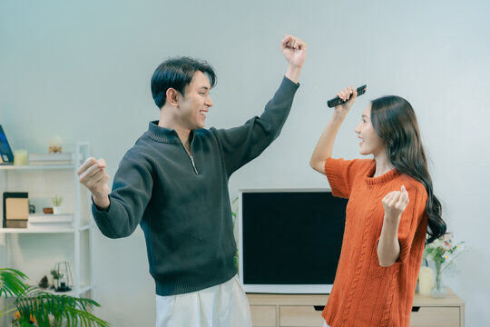 Happy Asian couple dancing and singing together in living room at home