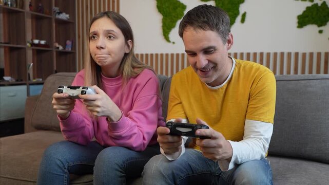 Couple playing video games at home on sofa, man and woman holding game controllers. Gamers, entertainment, and leisure together.