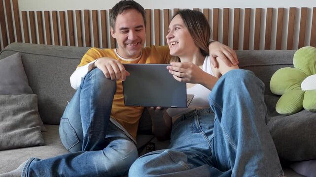 Boyfriend and girlfriend laughing while watching a funny video on a laptop at home. Online entertainment, humor, and joyful leisure together.