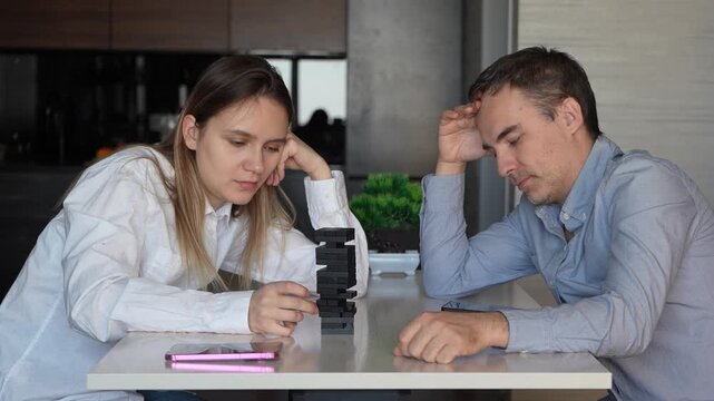 Couple playing a tense game of Jenga at a table, focusing on not knocking down the wooden tower. Concentration, family fun, and strategic thinking.