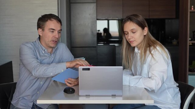 Tutor teaching student pointing at laptop screen. Two colleagues working on task together using computer and internet.