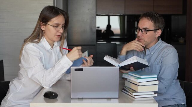 Woman and man studying at home: woman works on laptop, man reads a book. Home tutoring, distance learning, and exam preparation. the tutor teaches the student at home