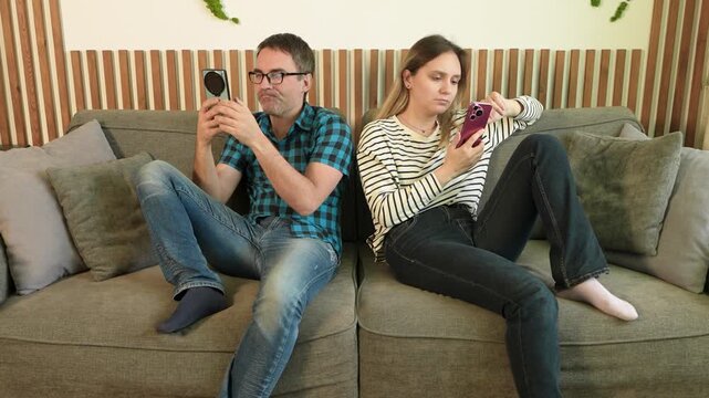 Couple sitting on a sofa, both looking at their smartphones, physically together but emotionally distant. Digital loneliness, screen addiction, and lack of real communication.