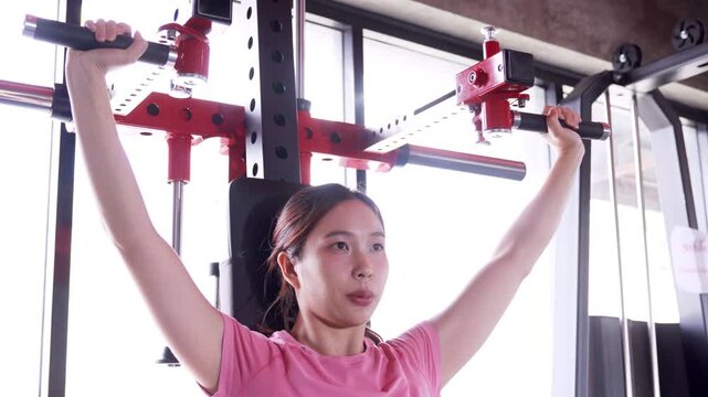 Young Asian woman performing shoulder press workout on gym machine during strength training session