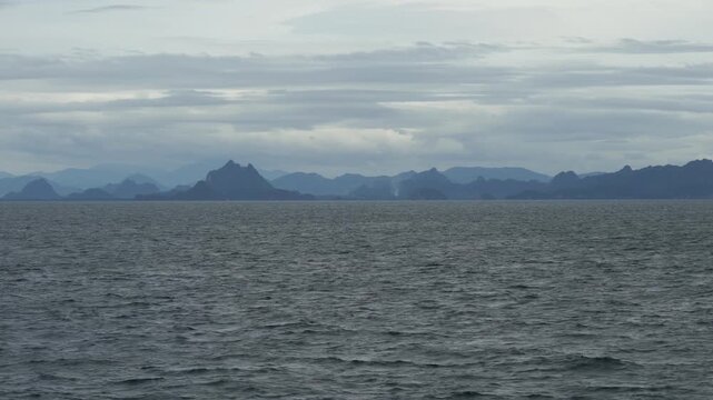 Panoramic view of the mountainous mainland coastline under heavy cloud cover, filmed from an approaching ferry in the Gulf of Thailand in Surat Thani, Thailand