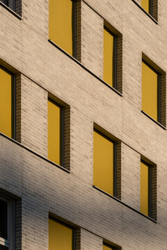 Contemporary brick building facade with yellow window shutters creating a repeating geometric pattern across the warm urban exterior