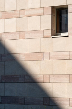 Minimal stone building facade with a single window and strong diagonal shadow creating geometric contrast across the exterior wall
