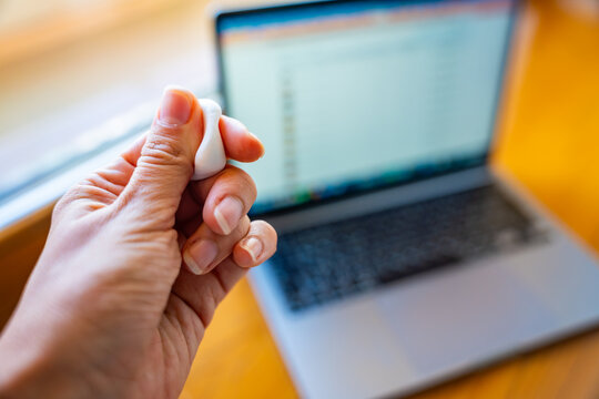 Woman squeezing stress relief putty while working at laptop. Sensory hand exercise helps reduce tension and manage stress during computer work