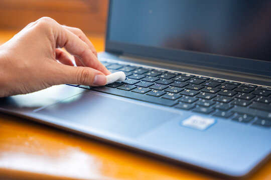 Hand pressing cleaning gel onto laptop keyboard to remove dust and debris. Keyboard cleaning compound collects dirt and particles between computer keys
