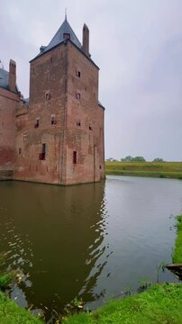 Historic medieval brick castle with moat and wooden drawbridge under cloudy sky