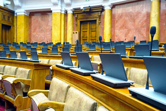 Empty seats with laptops and microphones in plenary chamber inside National Assembly, Belgrade. Conveys democratic process, government conference venue, and parliament interior before session.