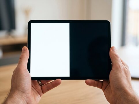 First-person view of male hands holding a digital tablet with a split black and white blank screen for app presentation and UI UX design mockup.