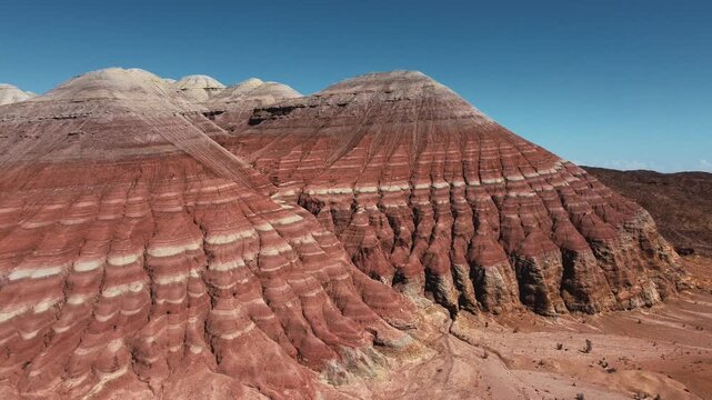 Aerial view of dramatic red and white striped sedimentary rock formations with layered erosion patterns under a clear blue sky in Aktau Mountains, Altyn Emel National Park, Kazakhstan