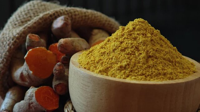 Turmeric powder in a wooden bowl with turmeric rhizomes.
