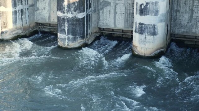 Water Cascading Over Concrete Rusty River Spillway Dam Lock Gate Hydroelectric Infrastructure, Swirling Dark Water Currents, and Waterway Engineering B-Roll. DAM river water dam gate.