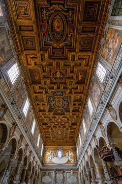 Ornate gilded coffered ceiling inside a grand Italian basilica with frescoes and chandeliers