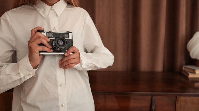 Young person holding a vintage camera, dressed in a white button-up shirt