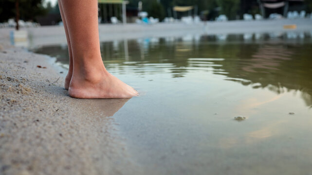 Child's bare feet touch the cool water at the edge of a sandy beach