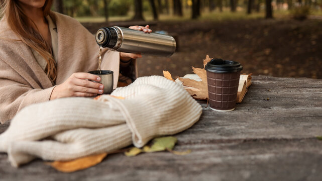 Cozy autumn scene with a woman pouring hot beverage from a thermos into a cup