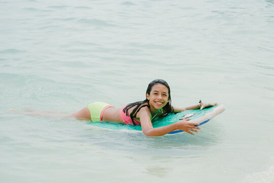 Young girl bodyboarding in tropical ocean enjoying summer vacation