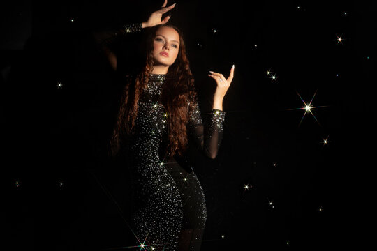 Woman in a sparkling gown among glowing stars on black, magic night and cosmic dream concept.