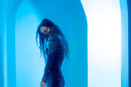 Contemporary dance movement, woman in a glittering gown bending in cyan light, motion concept.